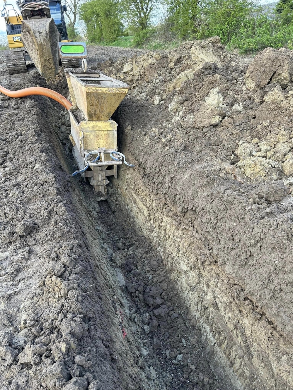 Gravemaskine i gang med at grave en rende til installation af dræningsrør på mark